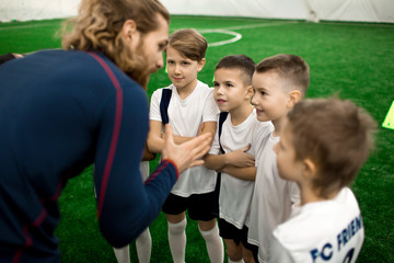 Young football trainer talking to team of little players on the field during break between games