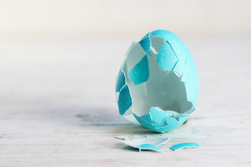 broken empty easter egg in turquoise on a white painted wooden background, concept for today's traditions and customs without the original sense, copy space