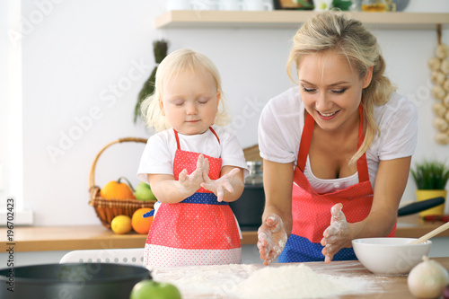 Plakat Mała dziewczynka i jej blondynki mama w czerwonych fartuchach bawić się i śmia się podczas gdy ugniatający ciasto w kuchni. Domowe ciasta na chleb, pizzę lub upiecz ciasteczka