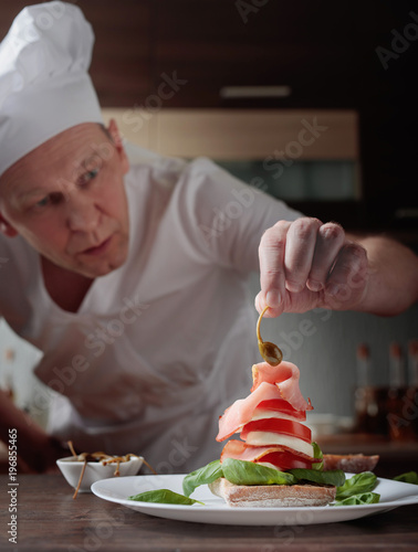 Fotoobraz na płótnie Szef kuchni przygotowuje przekąskę z mozzarellą i wędzonym mięsem.