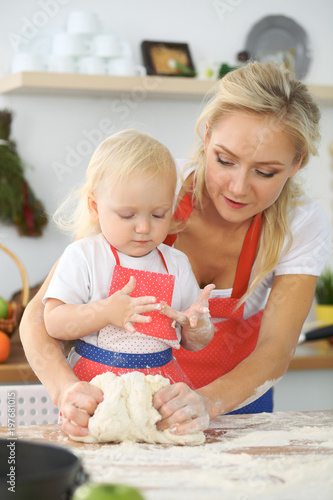 Plakat Mała dziewczynka i jej blondynki mama w czerwonych fartuchach bawić się i śmia się podczas gdy ugniatający ciasto w kuchni. Domowe ciasta na chleb, pizzę lub upiecz ciasteczka