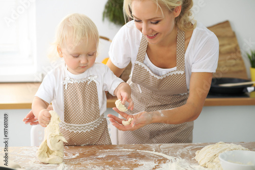 Plakat Mała dziewczynka i jej blondynki mama w czerwonych fartuchach bawić się i śmia się podczas gdy ugniatający ciasto w kuchni. Domowe ciasta na chleb, pizzę lub upiecz ciasteczka