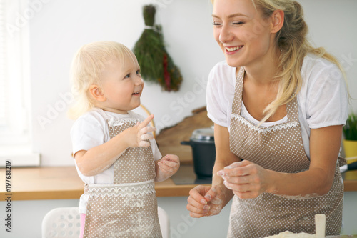 Plakat Mała dziewczynka i jej blondynki mama w czerwonych fartuchach bawić się i śmia się podczas gdy ugniatający ciasto w kuchni. Domowe ciasta na chleb, pizzę lub upiecz ciasteczka