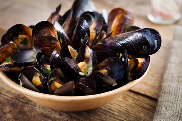 Black mussels on plate with green on wooden board