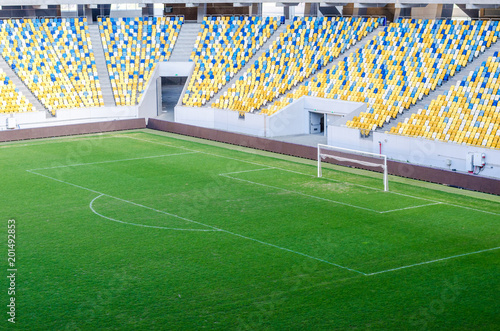 Plakat Siedzi fanów kolorowe plastikowe krzesła na tle stadionu piłkarskiego. Pusta stadium boiska piłkarskiego zielona trawa dla piłki nożnej atletyka areny.