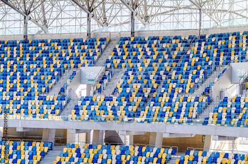 Plakat Siedzi fanów kolorowe plastikowe krzesła na tle stadionu piłkarskiego. Pusta stadium boiska piłkarskiego zielona trawa dla piłki nożnej atletyka areny.