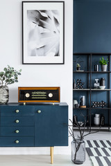 Painting, blue cabinet, retro radio, glass vase with branches, and metal shelf in the background