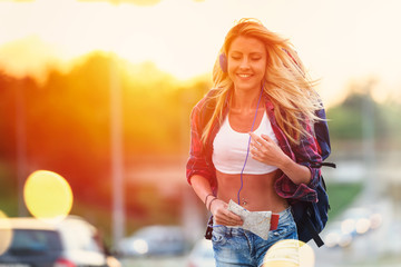 Beautiful young woman traveler with backpack walking along highway in sunset