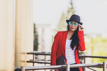 Portret of Happy hipster young woman with laptop wearing sunglasses, black hat and red jacket. Student girl with laptop in university campus. Toned image.
