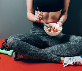 girl in sports clothes sitting near dumbbells and skipping rope with a plate of healthy breakfast in her hands