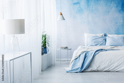 Фото: White lamp on a table in bright blue bedroom interior with bed against ombre wall White lamp on a table in bright blue bedroom interior with bed against ombre wall