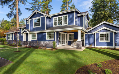 Beautiful luxury home exterior on sunny day with green grass, blue sky, and backdrop of trees