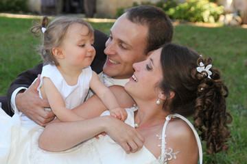 Bride And Groom With Bridesmaid daughter girl At Wedding day lying on grass