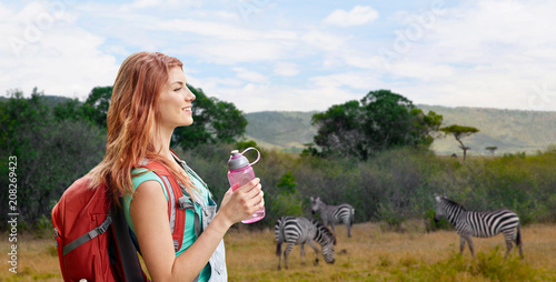 Фото: adventure, travel, tourism, hike and people concept - smiling young woman with backpack and bottle of water over zebras in african savannah background adventure, travel, tourism, hike and people concept - smiling young woman with backpack and bottle of water over zebras in african savannah background
