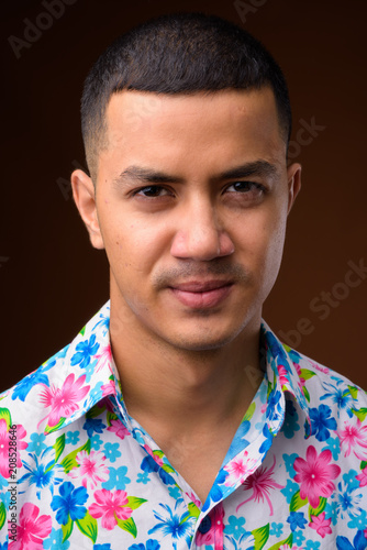 Фото: Young multi-ethnic Asian tourist man against brown background Young multi-ethnic Asian tourist man against brown background