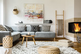 Wooden table next to grey corner settee in warm living room interior with painting and fireplace. Real photo