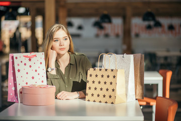 caucasian woman with shopping bags sitting at table and think or unhappy