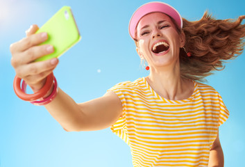 smiling fit woman against blue sky taking selfie with phone