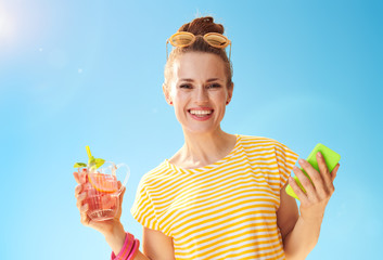 woman against blue sky with refreshing cocktail and smartphone