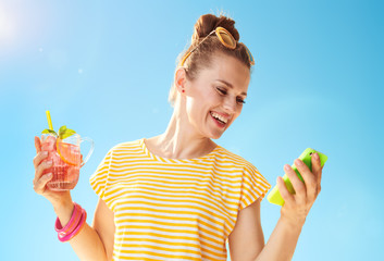 woman against blue sky with refreshing cocktail writing sms