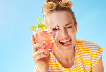 cheerful woman against blue sky with refreshing cocktail