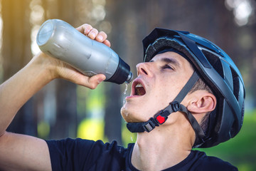 Cyclist in a helmet drinking water from a bottle while riding in the Park. Concept of active and healthy lifestyle