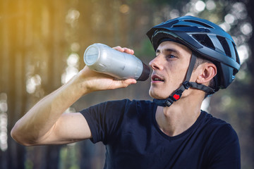 Cyclist in a helmet drinking water from a bottle while riding in the Park. Concept of active and healthy lifestyle