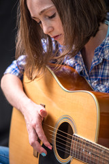 Girl teenager playing an acoustic guitar on a dark background in the Studio. Concert young musicians