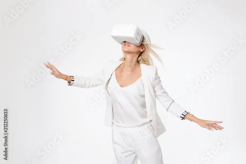 Фото: Blond woman in white suite with virtual reality goggles. Studio shot on white background Blond woman in white suite with virtual reality goggles. Studio shot on white background