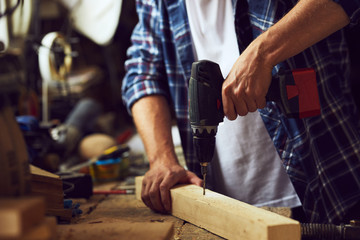 Carpenter working in his workshop with an electric drill into a wooden board