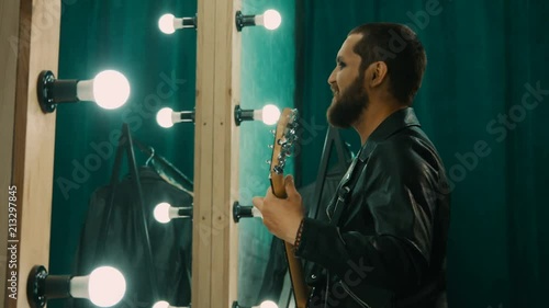 Видео: Side view of brutal man in leather jacket and with makeup playing guitar and preparing performance in front of mirror Side view of brutal man in leather jacket and with makeup playing guitar and preparing performance in front of mirror