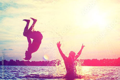 Glückliche junge Menschen laufen und springen am See beim Sonnenuntergang Glückliche junge Menschen laufen und springen am See beim Sonnenuntergang