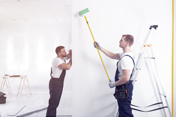Decorators painting a wall with a roller in a renovating office