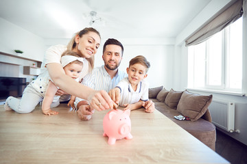 A smiling family saves money with a piggy bank. Happy family at the table in the room.