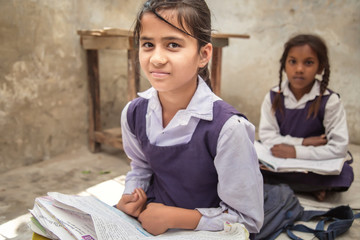 School girl in uniform of Indian Ethnicity sitting in their village classroom, looking at camera smiling.