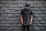 Handsome african american man in blank black t-shirt standing against brick wall