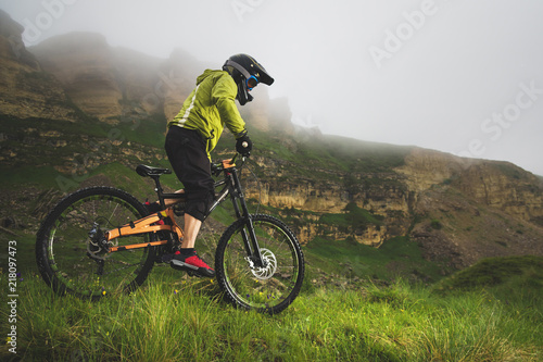 Foto obraz na płótnie canvas jednoczęściowy - A man in a mountain helmet riding a mountain bike rides around the beautiful nature in cloudy weather. downhill