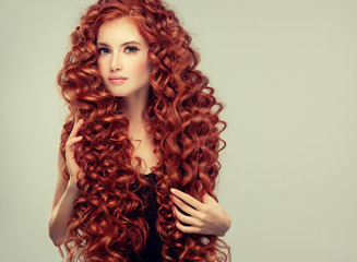 Beautiful model girl with long red curly hair .Red head . Care and beauty hair products 
