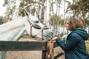 Beautiful young woman stroking the nose of a gray horse, love and care for animals