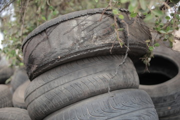 close up of a pile of used black dusty tires, outdoors, on street in the Gambia, with natural light with blue sky and green trees