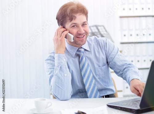 handsome businessman sitting at Desk and talking on a cell phone © ASDF