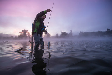 Man fishing in river with fly rod during summer morning.