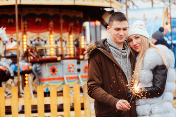 happy couple with christmas firelights walking in city holiday amusement park, carousel on background