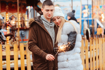 happy couple with christmas firelights walking in city holiday amusement park, carousel on background