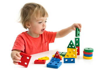 Charming infant boy sitting at table and playing with colorful constructor blocks isolated on white background