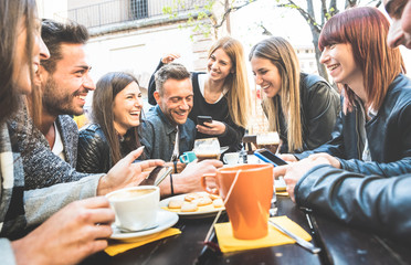Happy friends talking and having fun with mobile smart phones at restaurant drinking cappuccino and hot tea - Young people together at cafeteria - Friendship concept with men and women at coffee bar