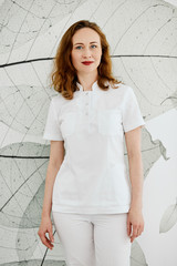 Pretty blond woman, doctor in medical uniform, smiling at the camera at the concrete wall background.