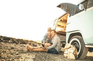 Hipster couple traveling together on oldtimer mini van transport - Travel lifestyle concept with indie people on minivan adventure trip having fun with mobile smart phone - Warm desaturated filter