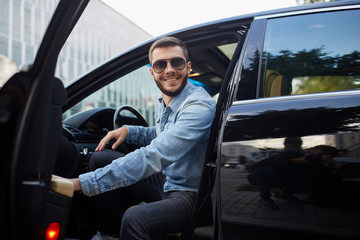 cheerful young brutal man looking at the camer while sitting in the car. close up photo.