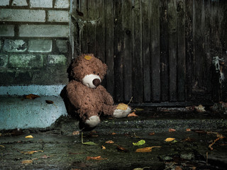 Sad wet plush bear on the background of textured old wooden wall